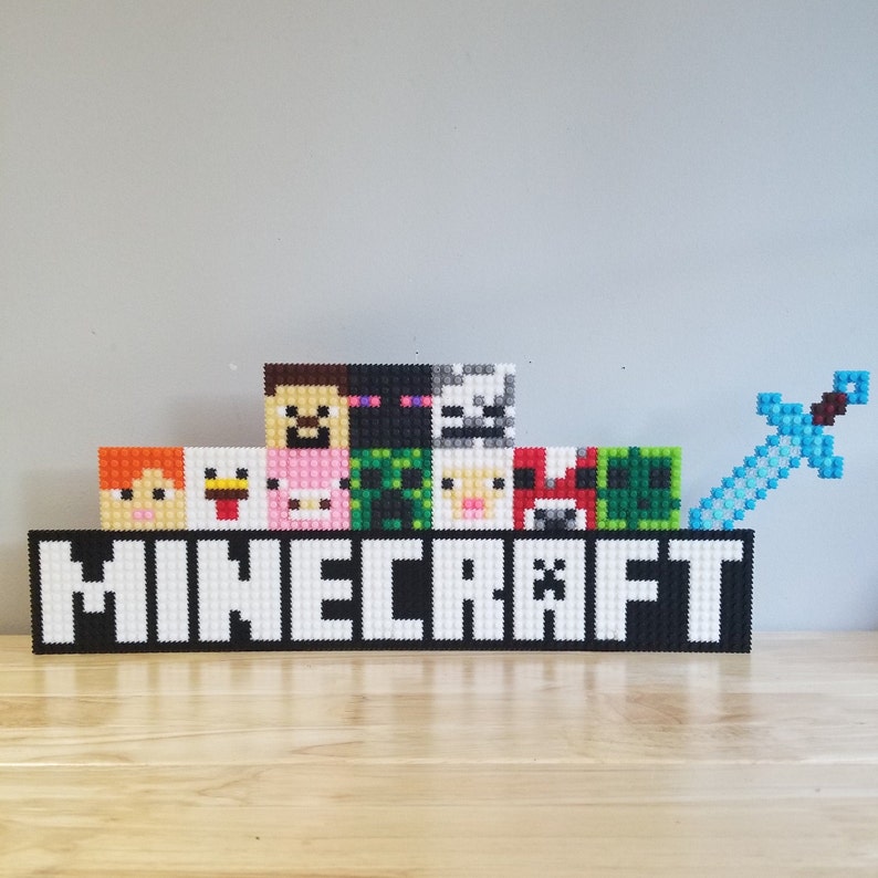 Puede incluir: Un logotipo de Minecraft en blanco y negro con la palabra "MINECRAFT" en letras blancas. Hay varios personajes pixelados del juego por encima del logotipo, incluyendo un cerdo, una gallina, un creeper y un esqueleto. Una espada pixelada azul est&aacute; a la derecha del logotipo.