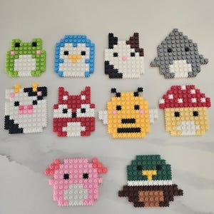 May include: A collection of ten colorful pixel art animal designs, including a frog, penguin, cow, shark, fox, bee, mushroom, axolotl, and duck. Each design is made of small, interlocking blocks in various colors.