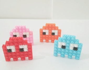 May include: Four small plastic Pac-Man figures in different colors: red, pink, orange, and blue. Each figure has white eyes and a black mouth.