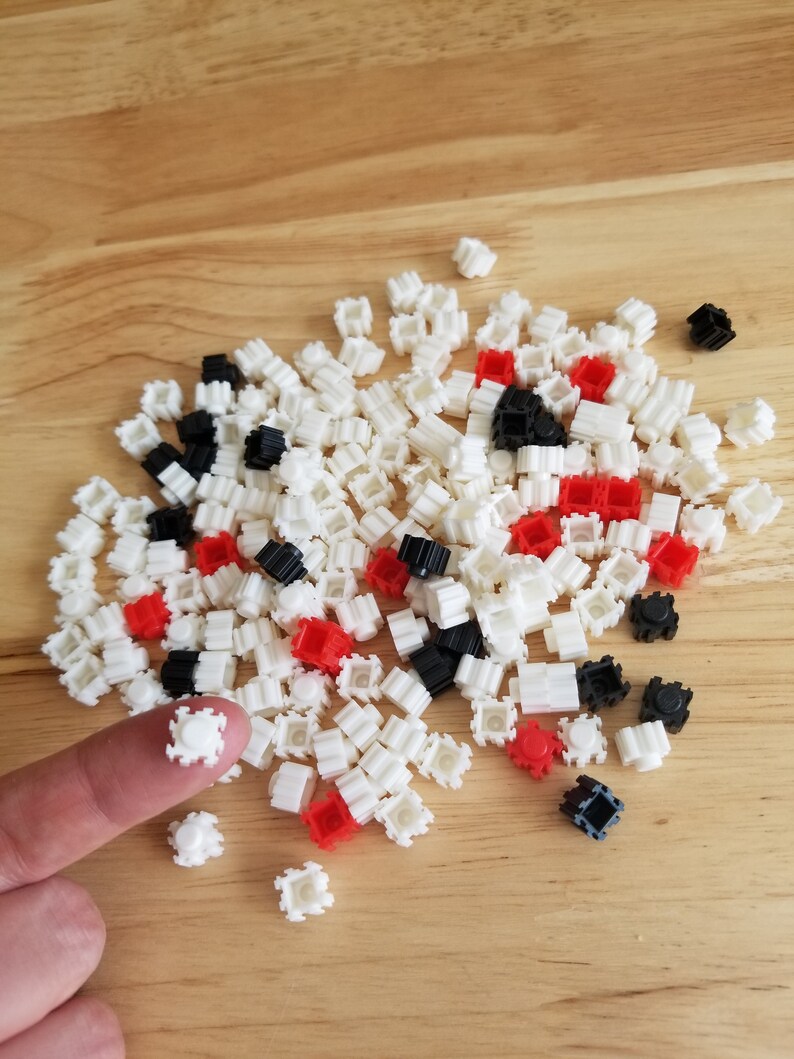 Puede incluir: Un mont&oacute;n grande de peque&ntilde;os bloques de construcci&oacute;n de pl&aacute;stico blanco con acentos rojos y negros. Un dedo sostiene uno de los bloques blancos.