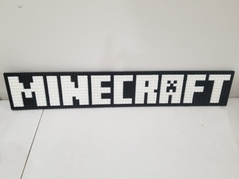 Puede incluir: Un logotipo de Minecraft en blanco y negro hecho de peque&ntilde;os cuadrados blancos sobre un fondo negro. El logotipo dice "MINECRAFT" con una cara de Creeper en la "A".