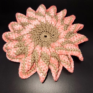 May include: A crocheted flower coaster in shades of pink and brown. The coaster is made with a spiral pattern and has a raised center.