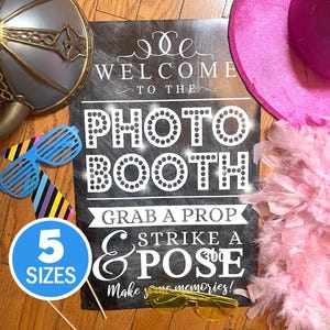 May include: A photo booth sign with the text "WELCOME TO THE PHOTO BOOTH" and "GRAB A PROP & STRIKE A POSE". Includes props like a pink hat, feather boa, and novelty glasses. A blue circle indicates "5 SIZES".