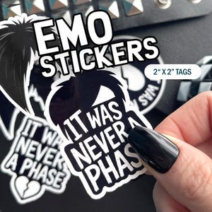May include: Black and white stickers with the text "EMO STICKERS" and "IT WAS NEVER A PHASE". The stickers are 2 inches by 2 inches and feature a stylized emo hairstyle and a broken heart graphic.
