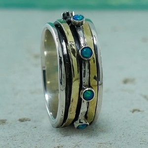 Può includere: Un anello girevole in argento e oro con quattro pietre preziose di opale blu. L'anello ha una finitura testurizzata e martellata.