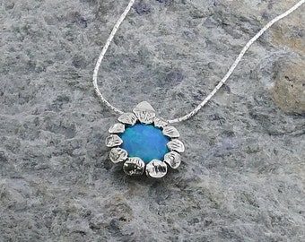 May include: A silver necklace with a blue opal pendant surrounded by a silver flower design.