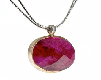 May include: A silver chain necklace with a pendant featuring a large, faceted ruby gemstone set in a gold bezel.