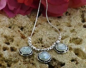 May include: A silver chain necklace with three round pendants featuring light blue and white Roman glass. The pendants are set in silver with a textured edge.