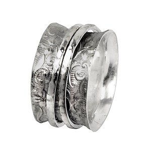 Könnte beinhalten: Ein silberner Drehring mit einem strukturierten Design. Der Ring hat eine breite Band und besteht aus mehreren Schichten, die sich frei drehen.