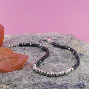 May include: A black and silver beaded bracelet with a silver clasp. The bracelet is made of small, square black beads and round silver beads.
