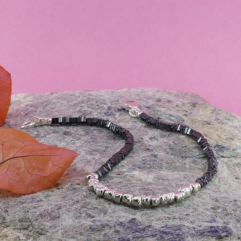 May include: A black and silver beaded bracelet with a silver clasp. The bracelet is made of small, square black beads and round silver beads.