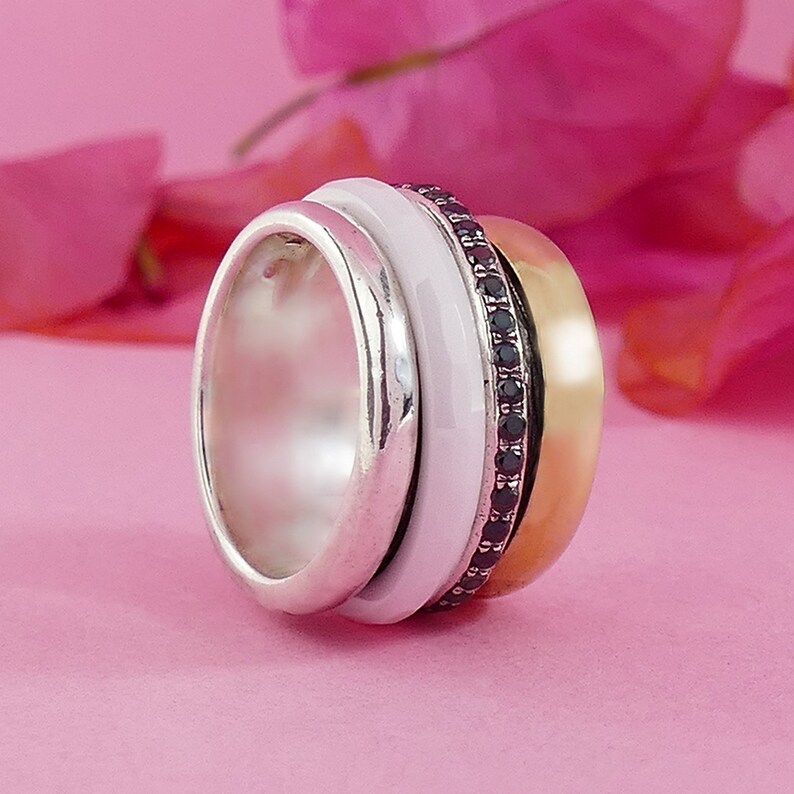 May include: A silver, white, and gold ring with a band of black gemstones. The ring is made of three bands that spin independently.