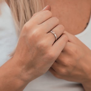 May include: A silver ring with a small, gold flower design. The ring is worn on the finger of a person's hand.