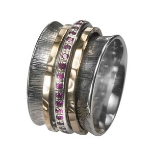 Op de afbeelding: Een draaibare ring van zilver en goud met een band van roze edelstenen. De ring is gemaakt van meerdere banden die om elkaar draaien.