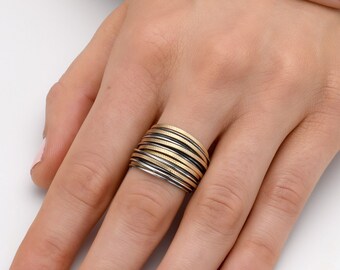 May include: A wide ring made of alternating bands of gold and silver metal. The ring is stacked with multiple bands, creating a unique and textured look.