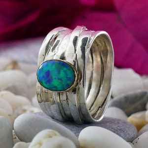 Peut inclure: Une bague en argent avec une opale verte et bleue sertie au centre. La bague est composée de plusieurs bandes d'argent torsadées et texturées.