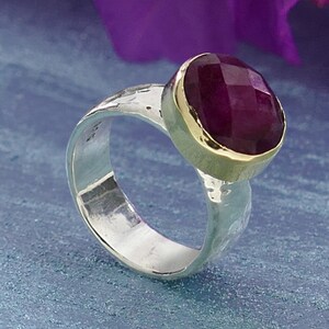 Op de afbeelding: Een zilveren ring met een gehammerde textuur en een gouden band met een grote, gefacetteerde, dieprode edelsteen.