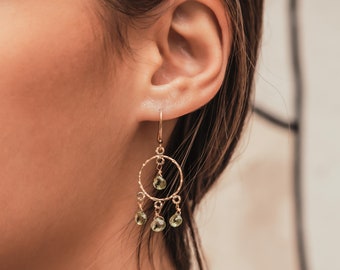 May include: Gold dangle earrings with a circle design and green gemstone accents.