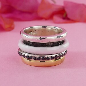 May include: A stack of four rings, one silver, one white, one black with black gemstones, and one gold. The rings are stacked on top of each other.