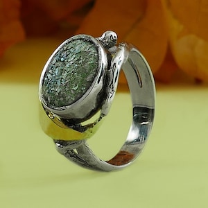 Peut inclure: Une bague en argent avec une pierre en verre vert sertie dans une bande torsadée. La bande est accentuée par une bande dorée.