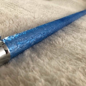 May include: A blue lightsaber with a textured handle and a silver metal hilt.