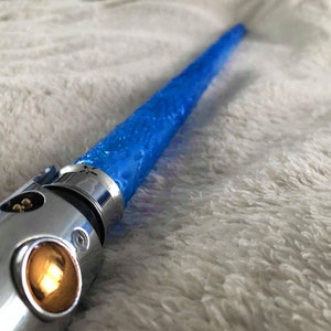 May include: A silver lightsaber hilt with a blue blade. The blade is textured and has a slight glow.