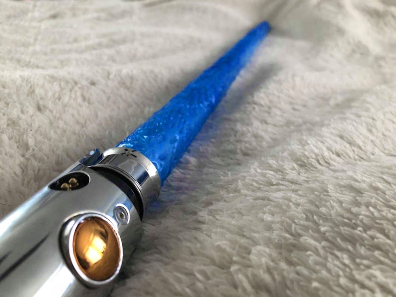 May include: A silver lightsaber hilt with a blue blade. The blade is textured and has a slight glow.