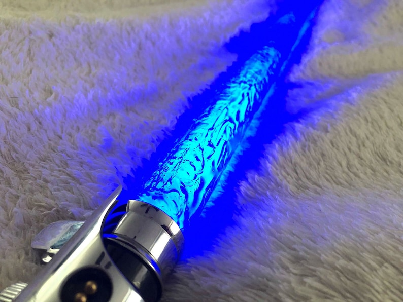 May include: A silver lightsaber with a blue blade. The blade has a textured, swirling pattern.