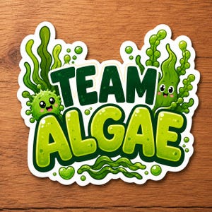May include: A die-cut sticker featuring the text TEAM ALGAE in bold, dark green and lime green letters. The design includes cartoonish green algae strands, bubbles, and two small, smiling, round green characters with large eyes and rosy cheeks.