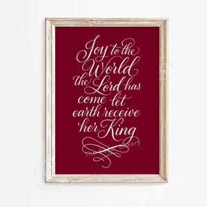 以下が含まれることがあります： 深紅の背景に「Joy to the World the Lord has come let earth receive her King」というテキストが白いエレガントな筆記体で書かれた額入りのプリント。明るい色の木製フレームに入っており、家の装飾に適しています。