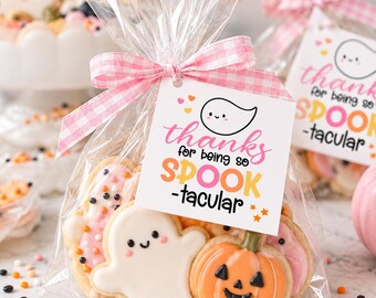 May include: A clear plastic treat bag filled with ghost and pumpkin shaped sugar cookies, tied with a pink and white gingham ribbon. A square white tag attached to the ribbon features a ghost illustration and the text thanks for being so SPOOK-tacular.