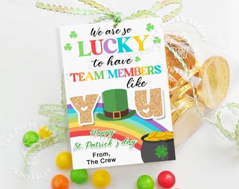 May include: A white gift tag with a rainbow and a pot of gold. The text on the tag reads "We are so LUCKY to have TEAM MEMBERS like YOU Happy St. Patrick's day From, The Crew".