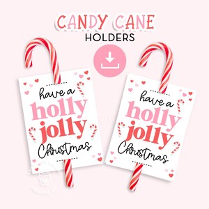 May include: Two candy cane holders with red and white striped candy canes. Each holder is a white rectangle with the text "have a holly jolly Christmas" in pink and red. The background is light pink.