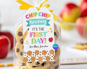 May include: A white gift tag with colorful text that reads "CHIP CHIP hooray IT'S THE FIRST DAY! Love Mrs Sanchez". The tag is attached to a clear plastic bag filled with chocolate chip cookies.