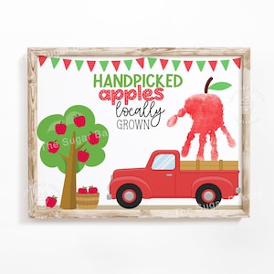 May include: A framed print featuring a red truck, apple tree, and a handprint apple. The text reads "Handpicked Apples Locally Grown" with a banner of red and green triangles. The artwork has a rustic, farmhouse style.