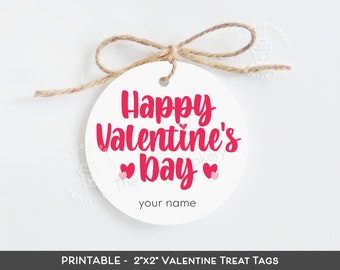以下が含まれることがあります： 2x2インチの丸いバレンタインデーのおやつタグ。ピンクの「Happy Valentine's Day」の文字と小さなピンクのハートが2つ。ハートの下に「your name」の文字があります。