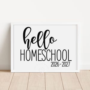 May include: A white rectangular frame containing a white sign with black text that reads hello HOMESCHOOL 2026-2027. The word hello is in a cursive script font, while HOMESCHOOL and the years are in a clean, sans-serif capital letter font.