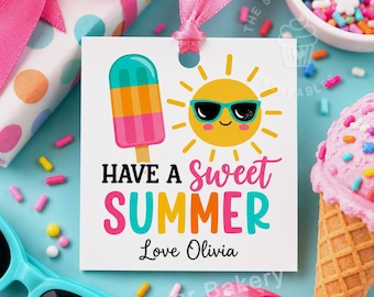 May include: A square white gift tag with a pink ribbon loop featuring a colorful popsicle, a yellow sun wearing teal sunglasses, and the text HAVE A SWEET SUMMER Love Olivia in black, pink, yellow, and teal lettering on a light blue background.