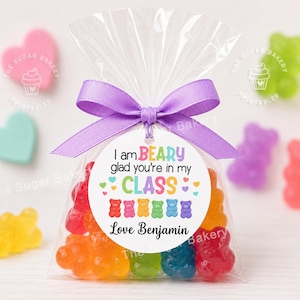May include: A clear cellophane bag filled with colorful gummy bears, tied with a purple ribbon and a circular tag. The tag reads "I am BEARY glad you're in my CLASS" with a row of bear illustrations and the name "Love Benjamin".