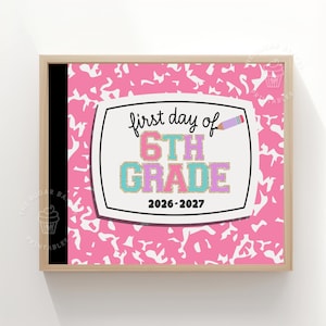 May include: A framed sign with a pink and white composition notebook pattern background. The center features a white label with the black text first day of 6TH GRADE, the years 2026-2027, and a small purple pencil graphic with gold glitter accents.