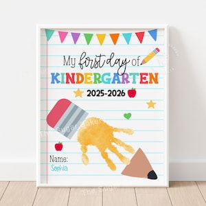 Peut inclure: Impression encadrée avec le texte "My first day of KINDERGARTEN 2025-2026" en lettres colorées. Le design comprend une empreinte de main, un crayon, une gomme, des étoiles et des illustrations de pommes. Le nom "Sophia" est écrit en bas.