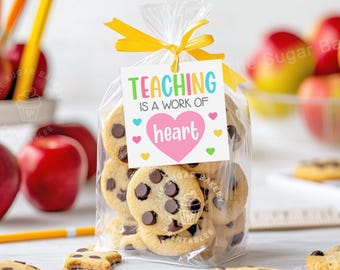 Könnte beinhalten: Eine durchsichtige Plastiktüte gefüllt mit Schokoladen-Chip-Cookies, die mit einem gelben Band und einem Geschenkanhänger mit der Aufschrift "TEACHING IS A WORK OF heart" gebunden ist.