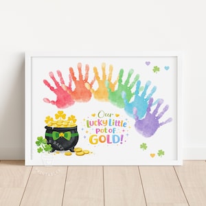 May include: A framed print featuring a rainbow of handprints arching over a black pot filled with gold coins and shamrocks. The text reads "Our lucky little pot of GOLD!" in colorful letters. Decorative hearts and shamrocks are scattered around the image.