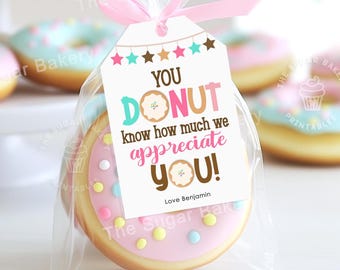 May include: A pink and white donut cookie with colorful sprinkles in a clear cellophane bag tied with a pink ribbon. A white gift tag with the text "You Donut know how much we appreciate you! Love Benjamin" is attached to the bag.