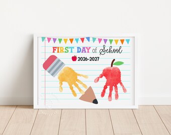 May include: A framed print featuring a lined paper background with colorful bunting at the top. The text reads FIRST DAY of School 2026-2027. It includes a yellow handprint shaped like a pencil and a red handprint shaped like an apple.