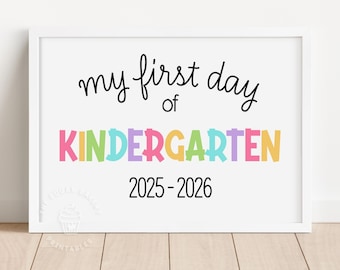 May include: A framed print with the text "my first day of Kindergarten" in black script above the word "KINDERGARTEN" in colourful block letters. The year "2025-2026" is printed below. The print is in a white frame.