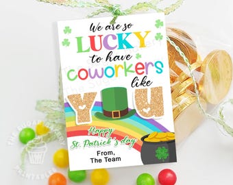May include: A St. Patrick's Day gift tag with the message "We are so LUCKY to have coworkers like YOU." The tag features a rainbow, a pot of gold, and a green leprechaun hat. The gift is tied with a green ribbon and surrounded by colorful candies.