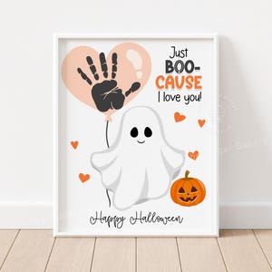 Op de afbeelding: Een ingelijste Halloween-print met een cartoongeest die een ballon met een handafdruk vasthoudt. De tekst luidt "Just BOO-CAUSE I love you!" met oranje harten en een pompoen. De woorden "Happy Halloween" staan onderaan.