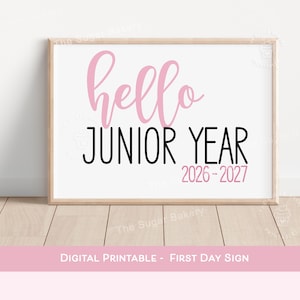 May include: A rectangular sign in a light wood frame featuring the text hello in a pink script font, followed by JUNIOR YEAR in a bold black sans-serif font, and the years 2026-2027 in a smaller pink sans-serif font on a white background.