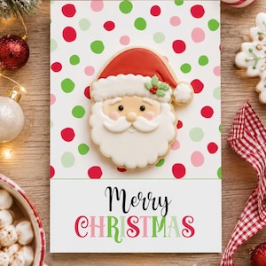 Pode incluir: Um cartão de felicitações retangular com uma bolacha de Pai Natal com gorro vermelho e barba branca sobre um fundo branco com pintas vermelhas, verdes e cor-de-rosa. A parte inferior apresenta o texto Merry CHRISTMAS a preto e vermelho.